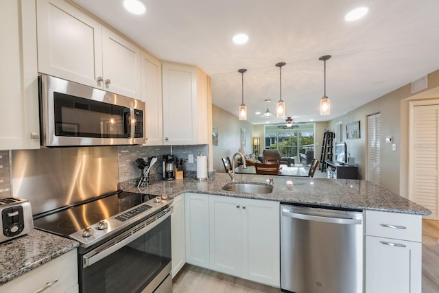 kitchen featuring sink, light stone counters, appliances with stainless steel finishes, kitchen peninsula, and backsplash