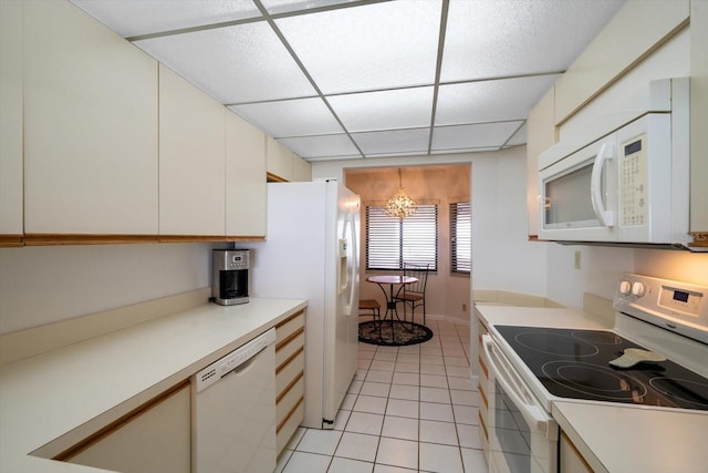 kitchen with a paneled ceiling, white appliances, light tile patterned floors, white cabinetry, and a notable chandelier