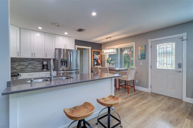 kitchen with tasteful backsplash, white cabinets, stainless steel fridge, hanging light fixtures, and light hardwood / wood-style floors