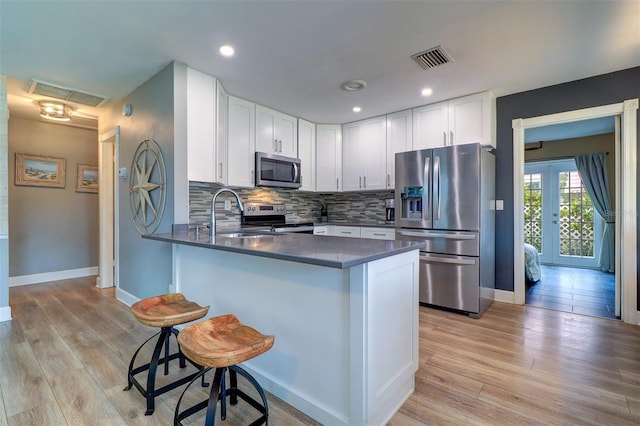 kitchen with stainless steel appliances, white cabinets, kitchen peninsula, backsplash, and light hardwood / wood-style floors