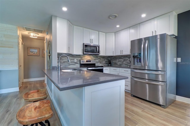 kitchen with decorative backsplash, light hardwood / wood-style floors, appliances with stainless steel finishes, and white cabinets