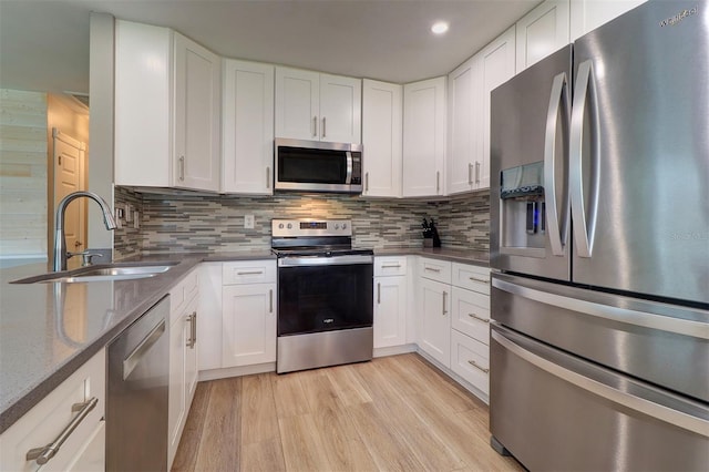 kitchen with white cabinetry, stainless steel appliances, sink, light hardwood / wood-style floors, and backsplash