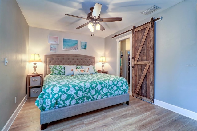 bedroom with wood-type flooring, a barn door, and ceiling fan