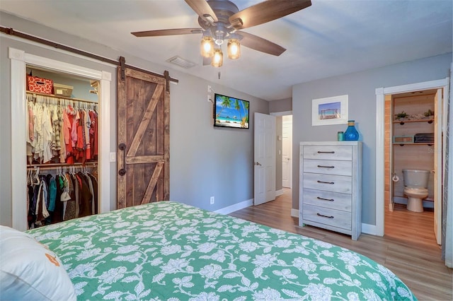 bedroom with ensuite bath, ceiling fan, wood-type flooring, and a barn door