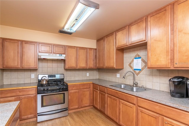 kitchen featuring light wood-type flooring, decorative backsplash, sink, and stainless steel gas range