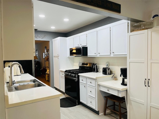 kitchen with black range with gas stovetop, white cabinetry, sink, and light hardwood / wood-style flooring