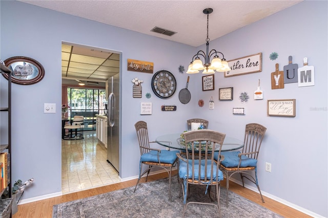 dining area with wood-type flooring, a textured ceiling, and an inviting chandelier