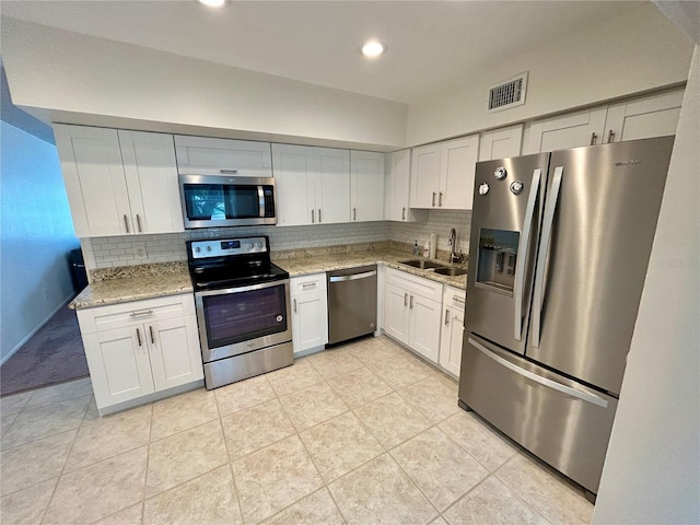 kitchen featuring sink, light stone counters, backsplash, white cabinets, and appliances with stainless steel finishes