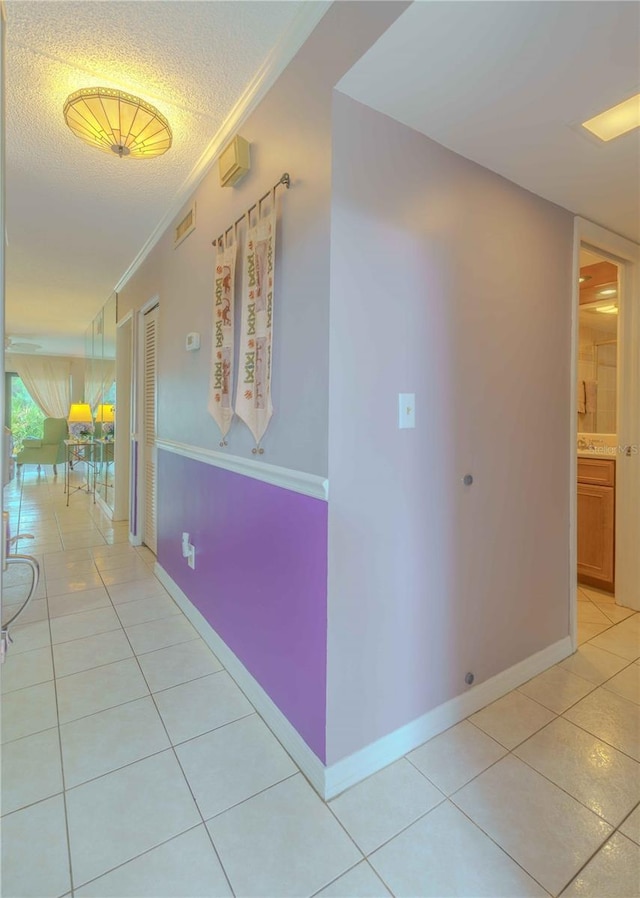 hall with crown molding, light tile patterned floors, and a textured ceiling