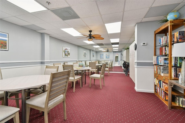 carpeted dining area with a paneled ceiling and ceiling fan