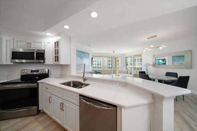 kitchen featuring stainless steel appliances, a peninsula, a sink, open floor plan, and light wood-type flooring