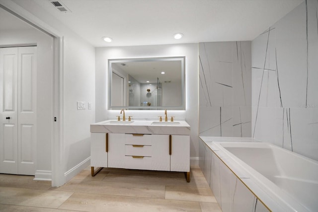 bathroom featuring double vanity, hardwood / wood-style floors, and tiled tub