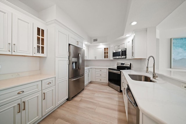 kitchen with light wood finished floors, white cabinetry, appliances with stainless steel finishes, and a sink