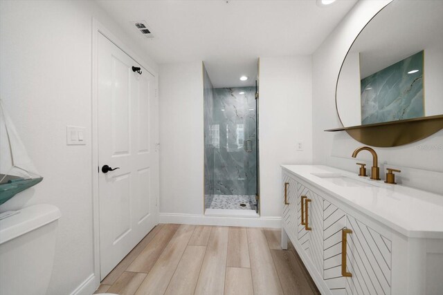 bathroom featuring wood-type flooring, a shower with door, toilet, and vanity