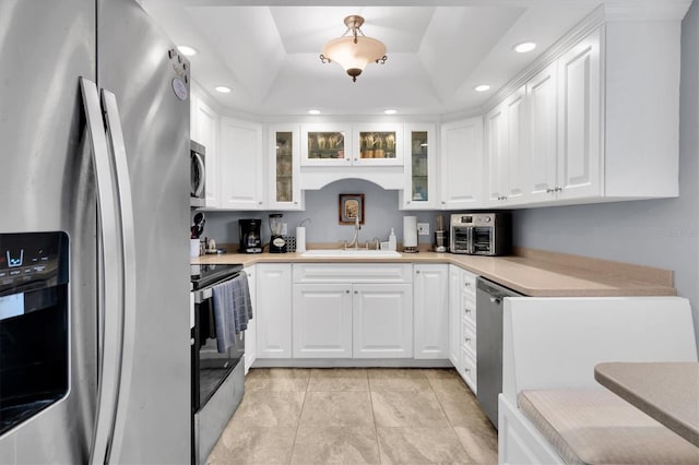 kitchen featuring sink, a tray ceiling, light tile patterned flooring, white cabinetry, and stainless steel appliances