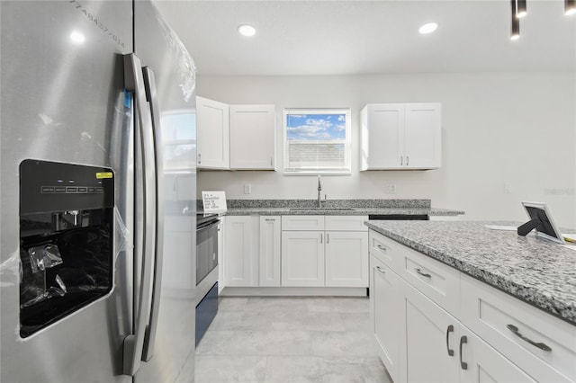 kitchen with light stone countertops, white cabinets, stainless steel fridge, and sink