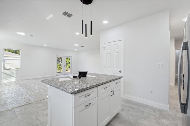 kitchen with white cabinetry, decorative light fixtures, french doors, light stone countertops, and a center island