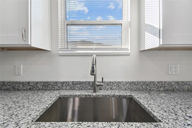 details featuring white cabinets, sink, and light stone counters