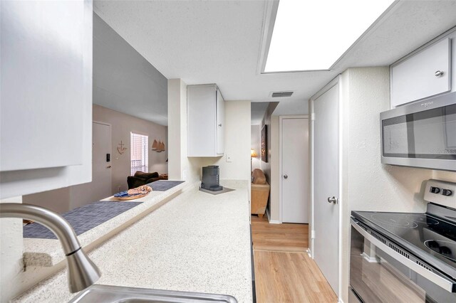 kitchen with white cabinetry, light hardwood / wood-style flooring, a textured ceiling, stainless steel appliances, and sink