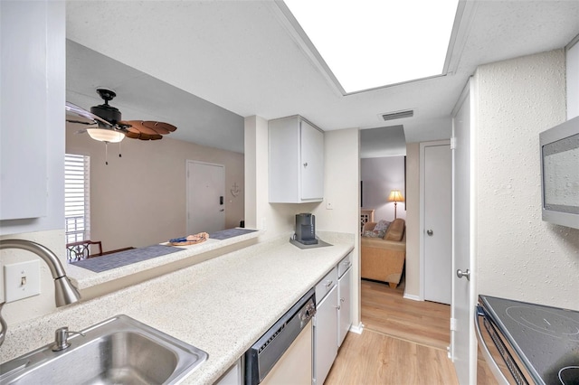 kitchen with a skylight, white cabinets, light wood-type flooring, stainless steel appliances, and sink