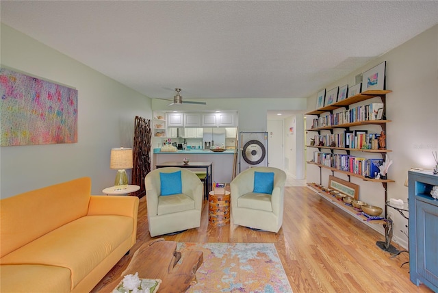 living room featuring ceiling fan, light hardwood / wood-style flooring, a textured ceiling, and washer / dryer