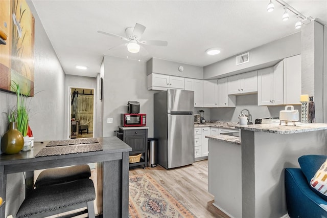 kitchen with white cabinets, light hardwood / wood-style floors, light stone counters, kitchen peninsula, and stainless steel refrigerator