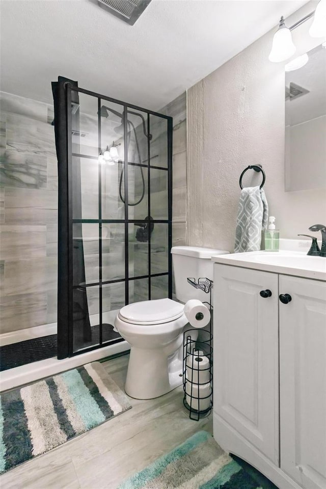 bathroom with toilet, hardwood / wood-style floors, vanity, and tiled shower