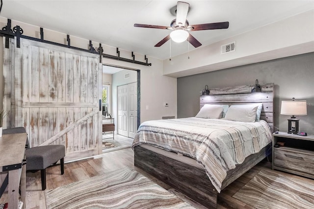 bedroom with a barn door, light hardwood / wood-style flooring, a closet, and ceiling fan