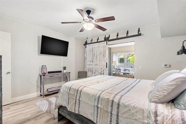 bedroom with a barn door, ceiling fan, and light wood-type flooring