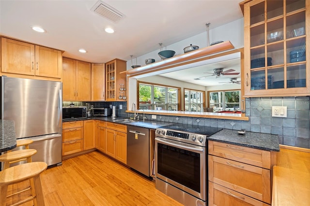 kitchen featuring backsplash, dark stone counters, appliances with stainless steel finishes, light hardwood / wood-style floors, and kitchen peninsula