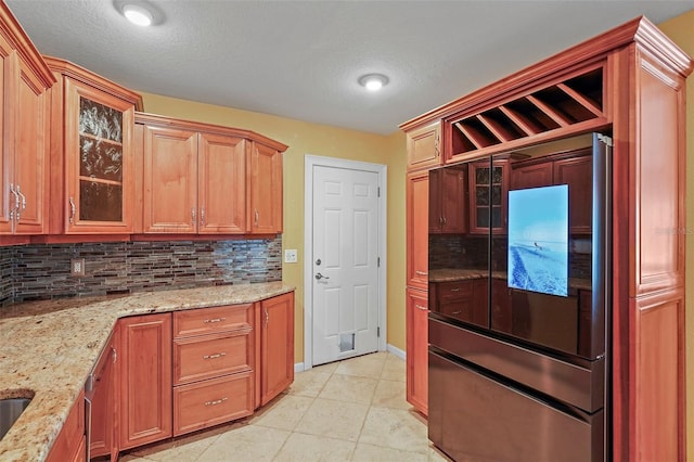 kitchen with backsplash, light stone counters, light tile patterned flooring, and built in refrigerator