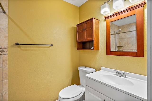 bathroom featuring a tile shower, vanity, and toilet