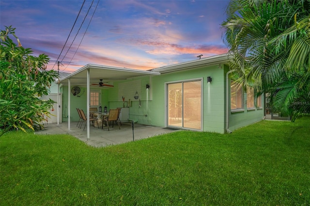 back house at dusk featuring a patio area, ceiling fan, and a yard