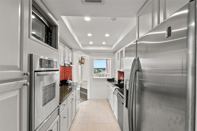 kitchen with a tray ceiling, light tile patterned floors, white cabinets, and black appliances