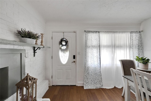 foyer with brick wall, dark wood-type flooring, and a textured ceiling