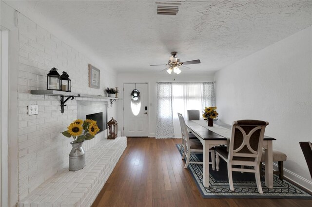 dining area featuring a brick fireplace, a textured ceiling, ceiling fan, and dark hardwood / wood-style flooring