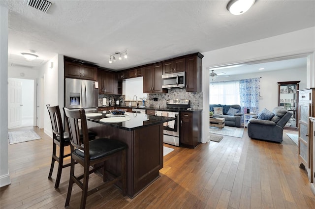 kitchen with dark wood-type flooring, stainless steel appliances, a breakfast bar, a center island, and tasteful backsplash