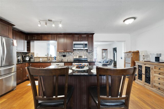 kitchen featuring light hardwood / wood-style floors, stainless steel appliances, dark brown cabinetry, and backsplash