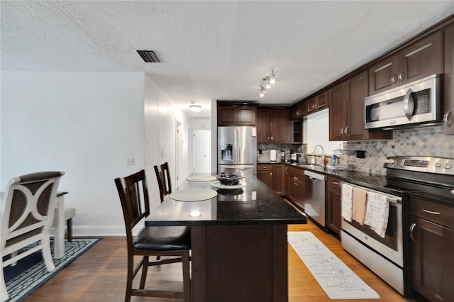 kitchen featuring a kitchen island, a breakfast bar area, stainless steel appliances, wood-type flooring, and sink