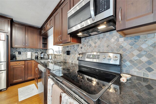 kitchen with decorative backsplash, light wood-type flooring, dark stone countertops, sink, and stainless steel appliances