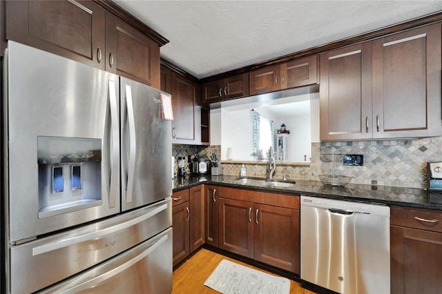 kitchen with tasteful backsplash, dark stone counters, light wood-type flooring, sink, and stainless steel appliances