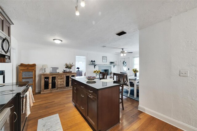 kitchen featuring dark brown cabinets, a breakfast bar area, ceiling fan, a kitchen island, and hardwood / wood-style flooring