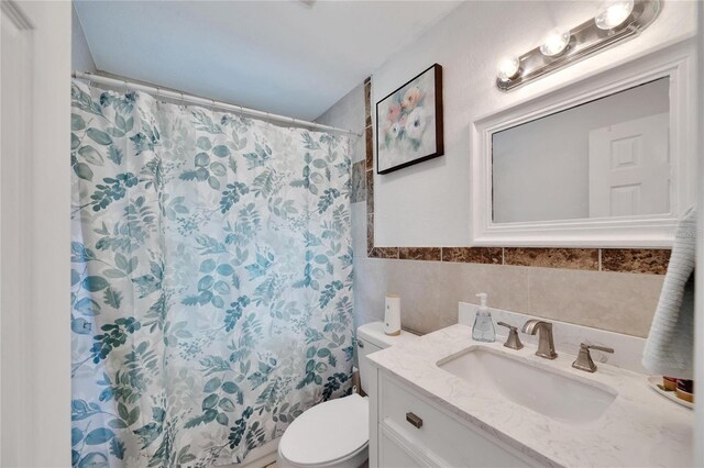 bathroom with toilet, curtained shower, vanity, and tile walls