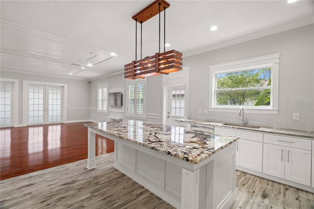 kitchen featuring sink, a kitchen island, decorative light fixtures, white cabinets, and light wood-type flooring