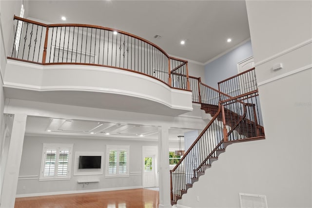 staircase featuring hardwood / wood-style floors, ornate columns, crown molding, and a high ceiling