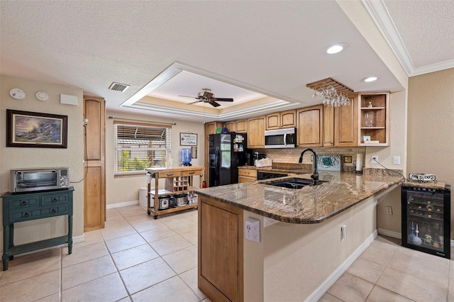 kitchen featuring sink, black refrigerator with ice dispenser, dark stone counters, kitchen peninsula, and a raised ceiling