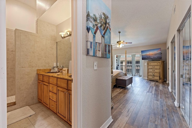 bathroom with wood-type flooring, tile walls, vanity, a textured ceiling, and ceiling fan