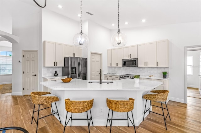 kitchen with sink, an island with sink, stainless steel appliances, and a high ceiling