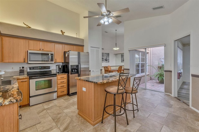 kitchen with stainless steel appliances, ceiling fan, sink, high vaulted ceiling, and a kitchen island