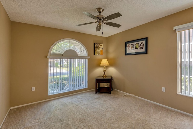 empty room with ceiling fan, a healthy amount of sunlight, light colored carpet, and a textured ceiling